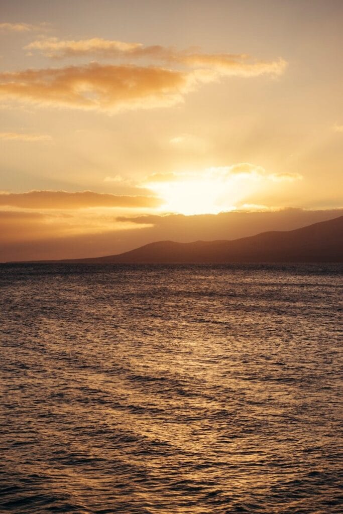 Golden sunset over the ocean with distant hills.